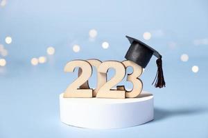 Class of 2023 concept. Wooden number 2023 with graduated cap on podium on colored background photo