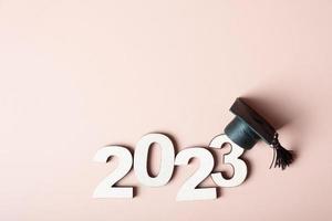 Class of 2023 concept. Wooden number 2023 with graduated cap on colored background photo