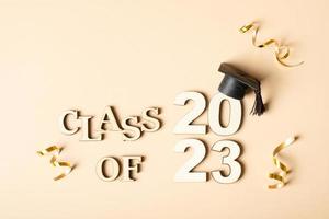 Class of 2023 concept. Wooden number 2023 with graduated cap on beige background photo