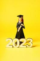 Class of 2023 concept. Wooden number 2023 with graduate statuette on color background photo