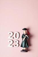 Class of 2023 concept. Wooden number 2023 with graduate statuette on color background photo