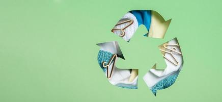 Colorful clothes and mini hungers under paper cut recycling symbol. Second hand, clothing donation and recycling concept photo