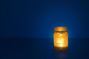 Glass jar with candle flame in the shape of a heart in the dark photo