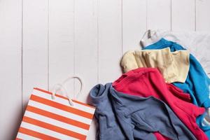 Colorful clothing and shopping bag on wooden background. Second hand, recycling concept photo
