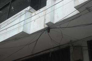 Messy tied up black electrical cable wires outside on the roof isolated on rusty old aged white walls. photo