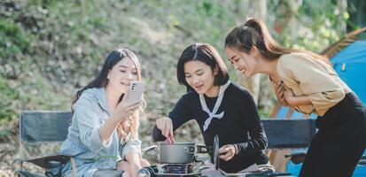 las mujeres jóvenes cocinan y usan el teléfono inteligente toman fotos en el campamento