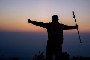 Silhouette of cheering hiking man open arms to the sunrise stand on mountain photo