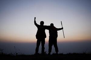 silueta de hombres que animan a los excursionistas abren los brazos al stand del amanecer en la montaña foto