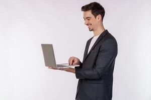 Portrait of young handsome smiling businessman holding laptop in hands, typing and browsing web pages isolated on white background photo