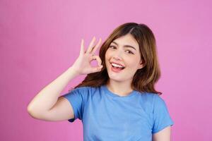 Portrait of happy young woman wearing casual t-shirt showing ok-sign ad solution good choice isolated over pink background photo