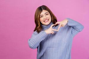 Portrait of Smiling young woman feels happy and romantic shapes heart gesture isolated over pink background photo