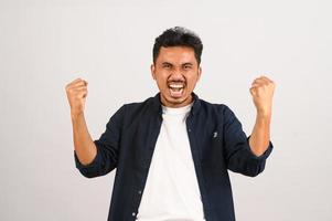 Portrait of Happy young asian man in blue shirt excited doing winner gesture with arm raised isolated on white background photo