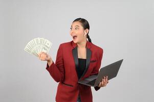 Young beautiful woman in formal clothing for officer hold banknote and laptop photo