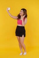 Portrait of Smiling young woman selfie with mobile phone in her hands while standing isolated over yellow background photo