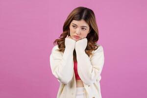 Portrait of beautiful young woman holding hands under chin and looking at something isolated over pink background photo