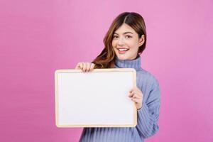 Portrait of Happy young woman holding an empty white placard over isolated pink background. photo