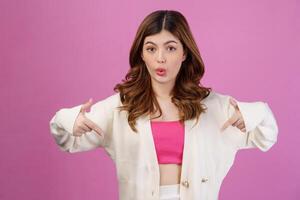 Portrait of Surprised young woman pointing to empty copy space for product over isolated pink background photo