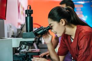 Asian young female farmer looking through a microscope in a laboratory. Modern technologies in agriculture management, agribusiness and research concept. photo