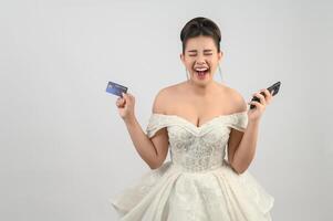 joven asiático hermosa novia destino con crédito tarjeta y teléfono inteligente en mano foto