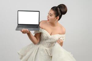 Young asian beautiful bride pose with mockup laptop computer in hand photo