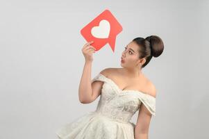 Asian beautiful bride smiling and posing with heart sign on white background photo