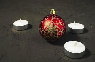 Decorative Christmas tree ball in red and gold color and flat candles on a dark background