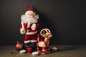 Santa Claus doll in a red suit with a candle, gifts, a Christmas ball and a Christmas deer photo