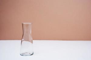 An empty glass vase on the table on a peach background photo