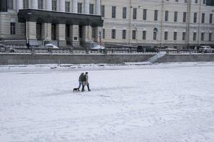 A couple of fashionable young city dwellers walk with a dog on the ice of the frozen city river photo