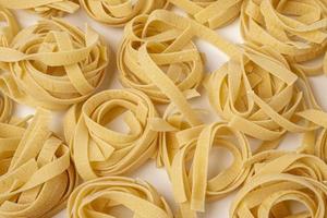 Raw tagliatelle , nest pasta, Egg pasta nests lying in a pattern on a white background photo