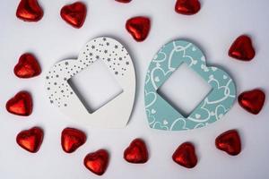 Two wooden colored empty heart-shaped photo frames and lots of shiny heart-shaped candies