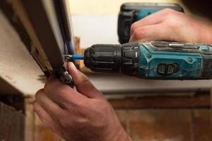 Drilling and installation of interior doors, the craftsman makes a hole in the door frame with a hand drill. photo