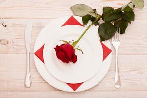 Top view of tableware of round and heart shaped empty plate, metal knife and fork served on white wooden table with glowing candle and gift box prepared for celebration of saint valentine day photo