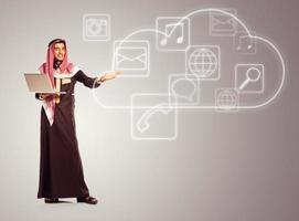 Young smiling arab with laptop shows virtual icons of the cloud service photo