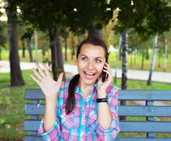 un retrato de un sonriente hermosa mujer en un parque hablando en el teléfono foto