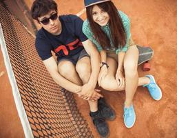 Couple sitting on a skateboard on the tennis court photo