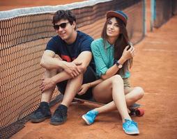 Pareja sentado en un patineta en el tenis Corte foto