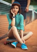 Girl sitting on a skateboard on the tennis court photo