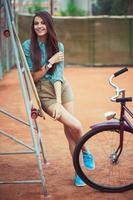 Beautiful young girl with longboard and bicycle standing on the tennis court photo