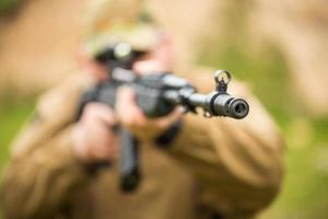 hombre en camuflaje con un escopeta puntería a un objetivo. atención en agujero foto