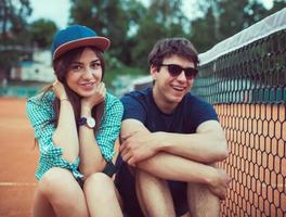 Young couple sitting on a skateboard on the tennis court photo