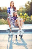 Two happy beautiful teen girls driving shopping cart outdoors photo