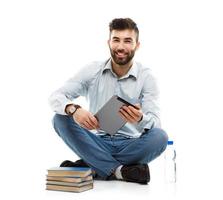 joven barbado sonriente hombre participación un tableta con libros y un botella de agua sentado en un blanco foto