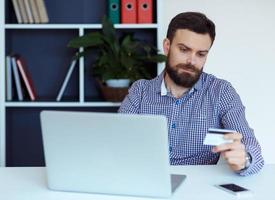 Young bearded man pays by credit card online shopping photo