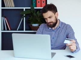 Young bearded man pays by credit card online shopping photo