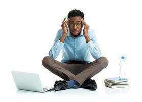 African american college student in stress sitting with laptop, books and bottle of water on white photo