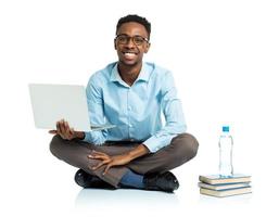 Happy african american college student with laptop, books and bottle of water sitting on white photo