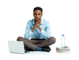 African american college student with laptop, books and bottle of water sitting on white photo