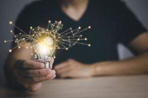 Businessman hand holding light bulb with icons and working on the desk, Creativity and innovation are keys to success.Concept of new idea and innovation with energy and power , working at home, photo