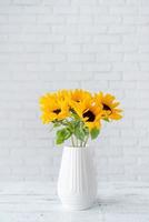 un ramo de flores de girasoles en un florero en contra el antecedentes de un blanco ladrillo pared foto